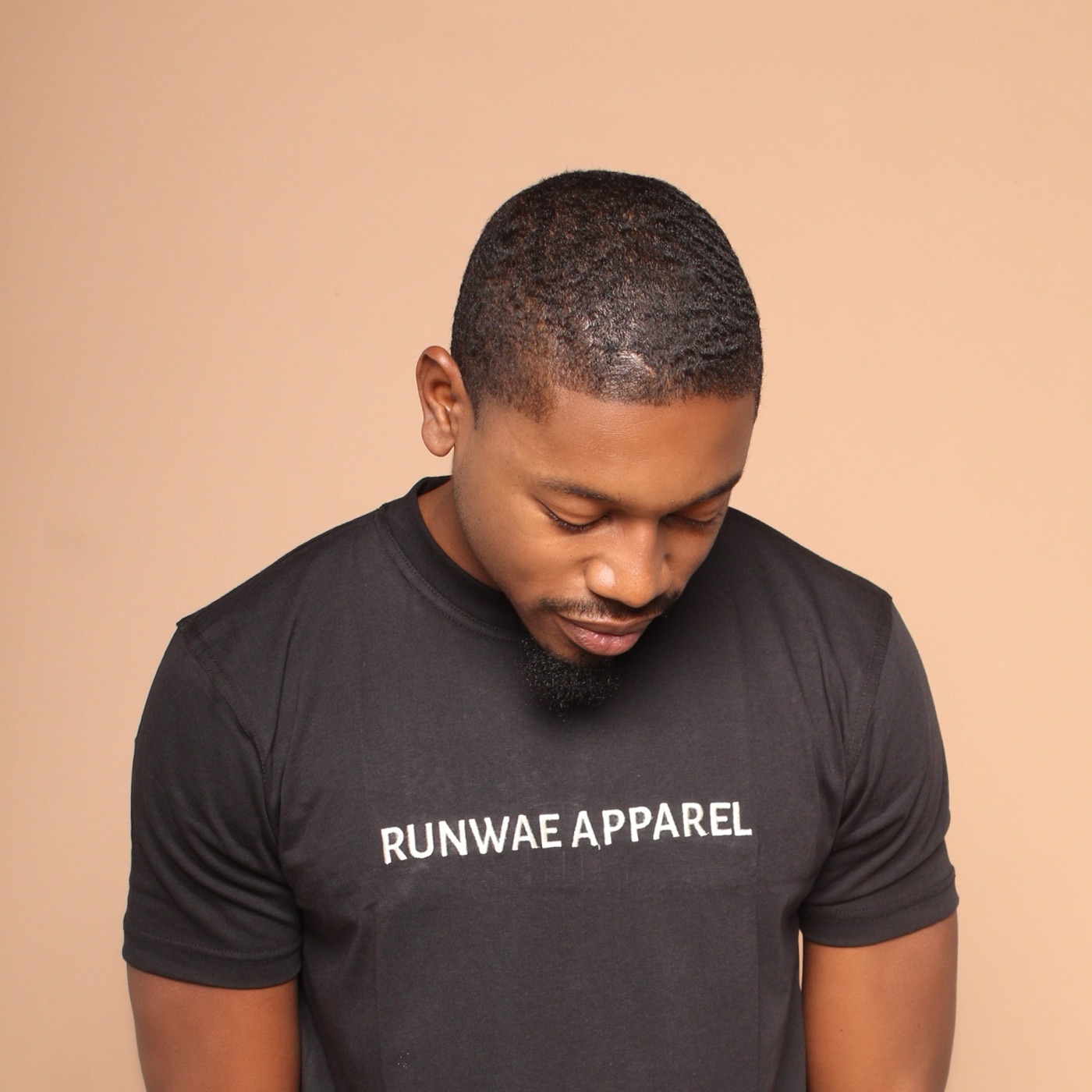 A man in a black RUNWAE APPAREL tee, looking down